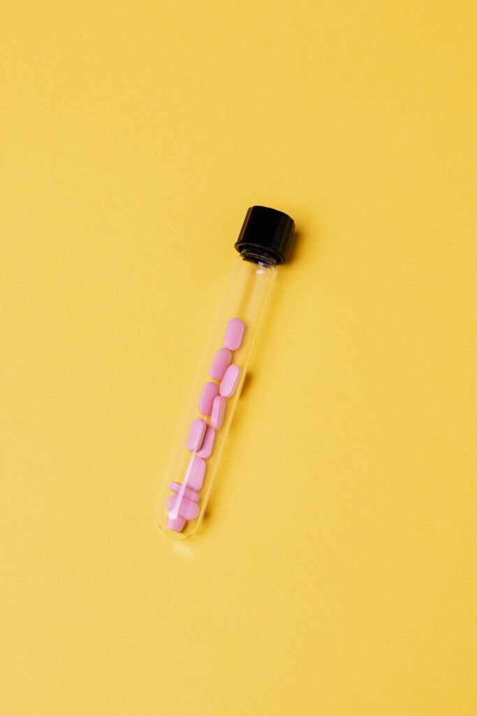 A test tube containing pink pills against a vibrant yellow background, depicting healthcare concepts.