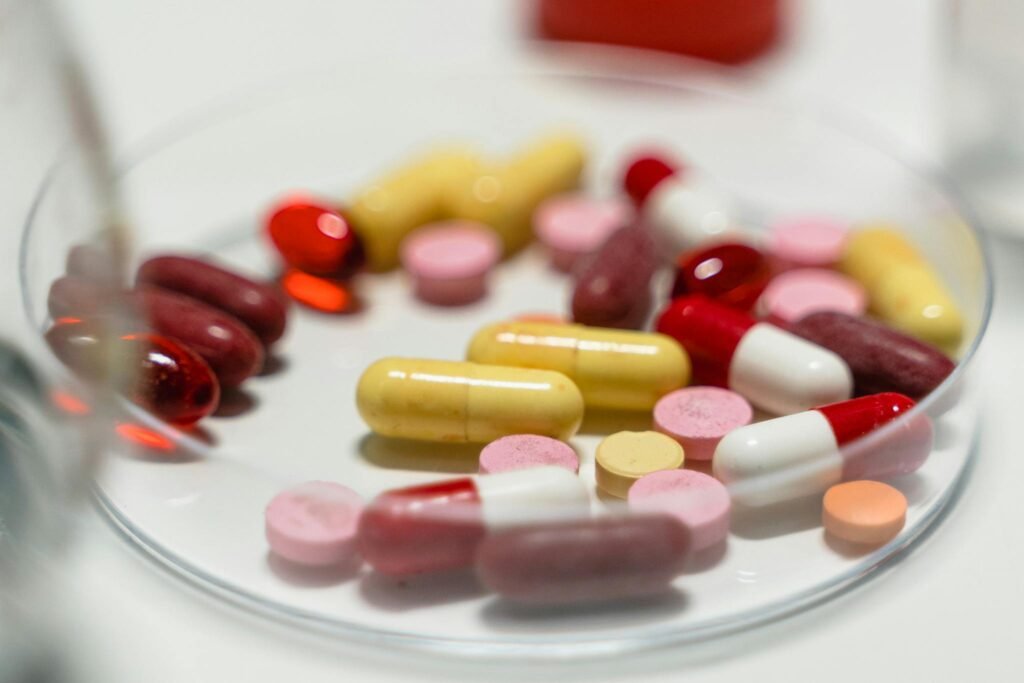 Assorted colorful pills and capsules arranged on a Petri dish for pharmaceutical analysis.